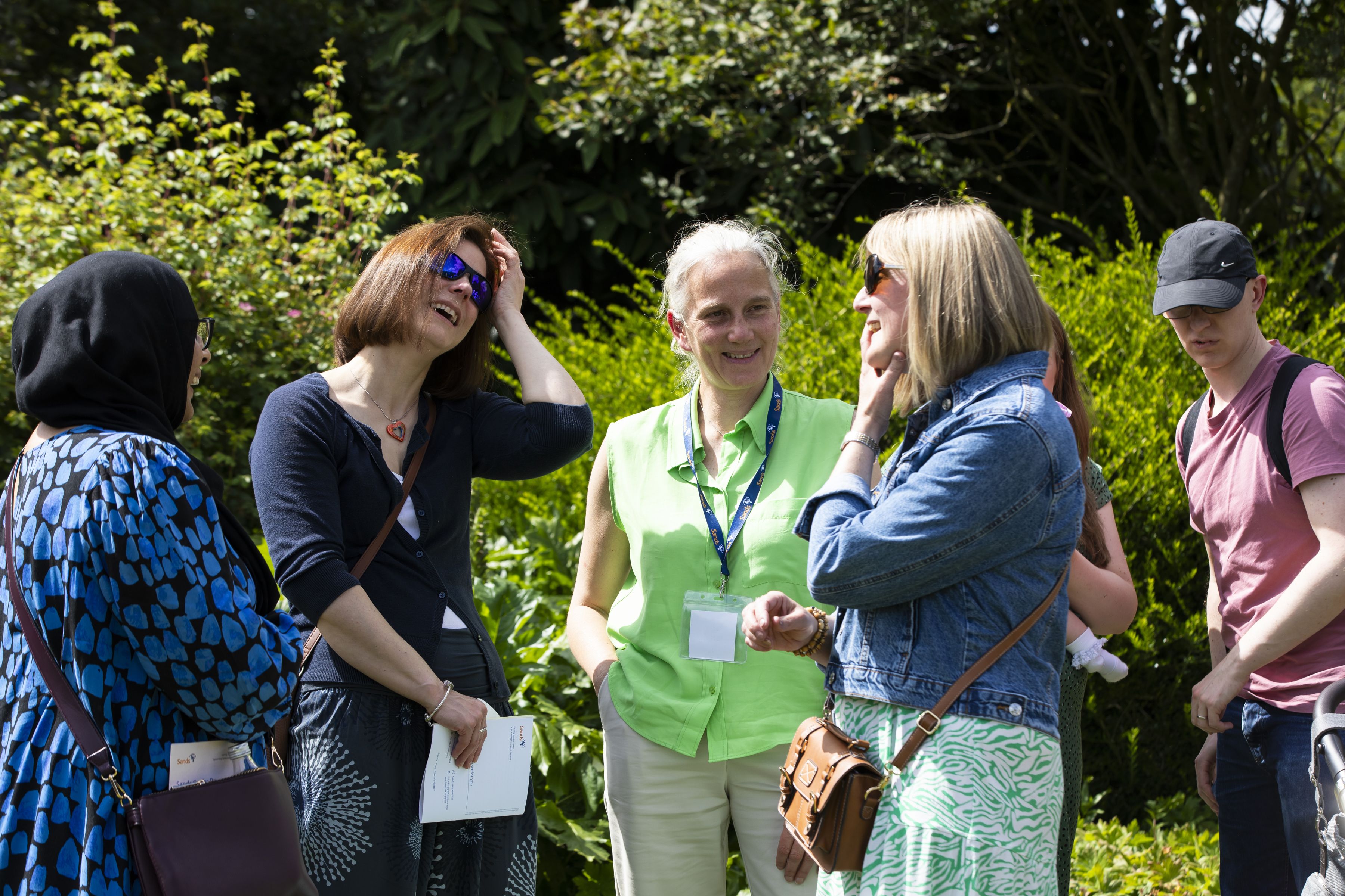 A group of people engaged in conversation whilst standing together in the Sands Garden at the National Memorial Arboretum.