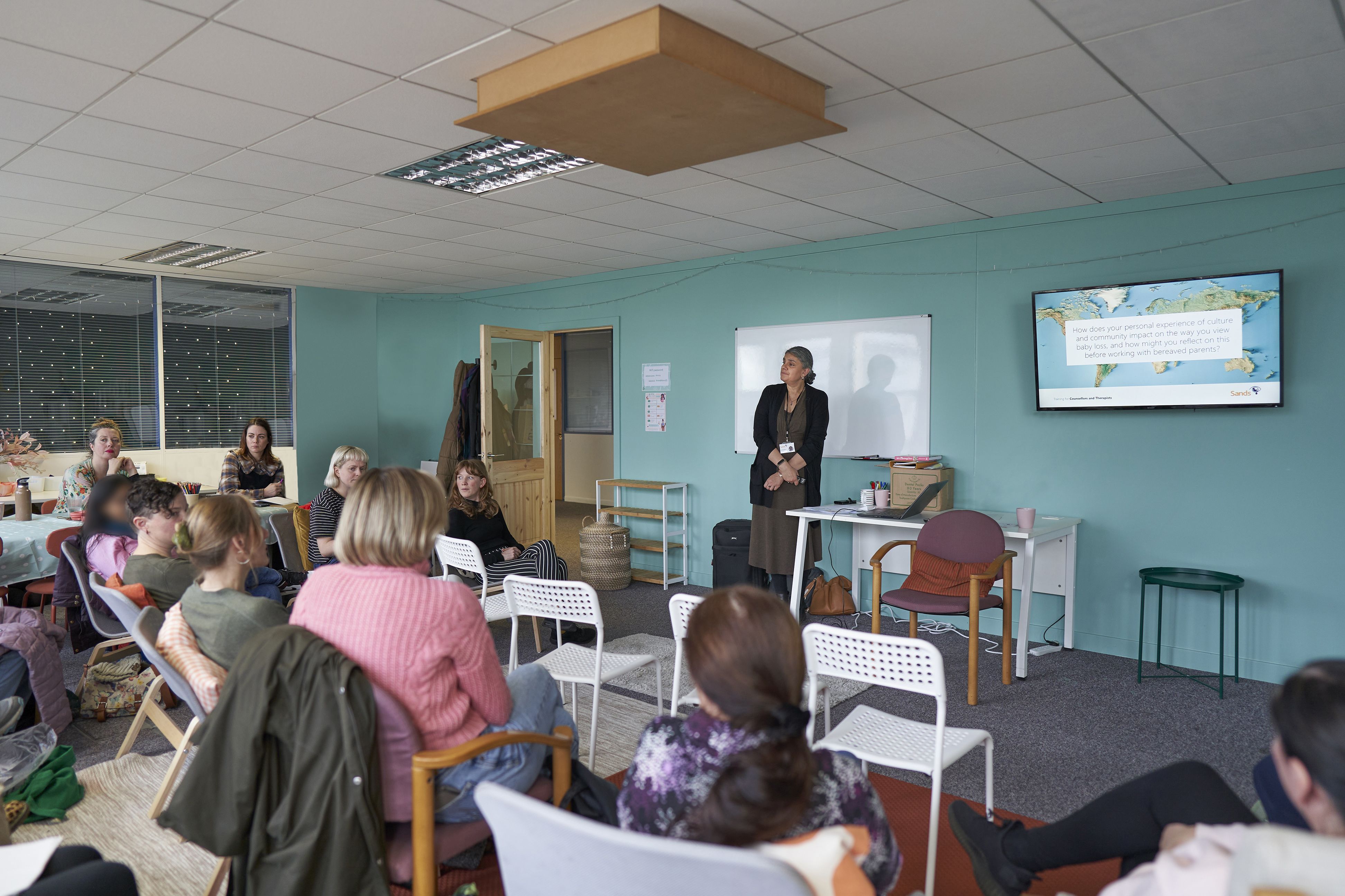 A Sands trainer is stood at the front of the room, delivering training to a group of people. 