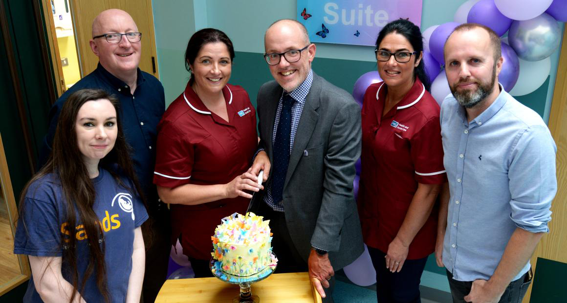 Sands Staff and Nurses unveiling the new bereavement suite at Craigavon Area Hospital. They are standing together and cutting a cake.