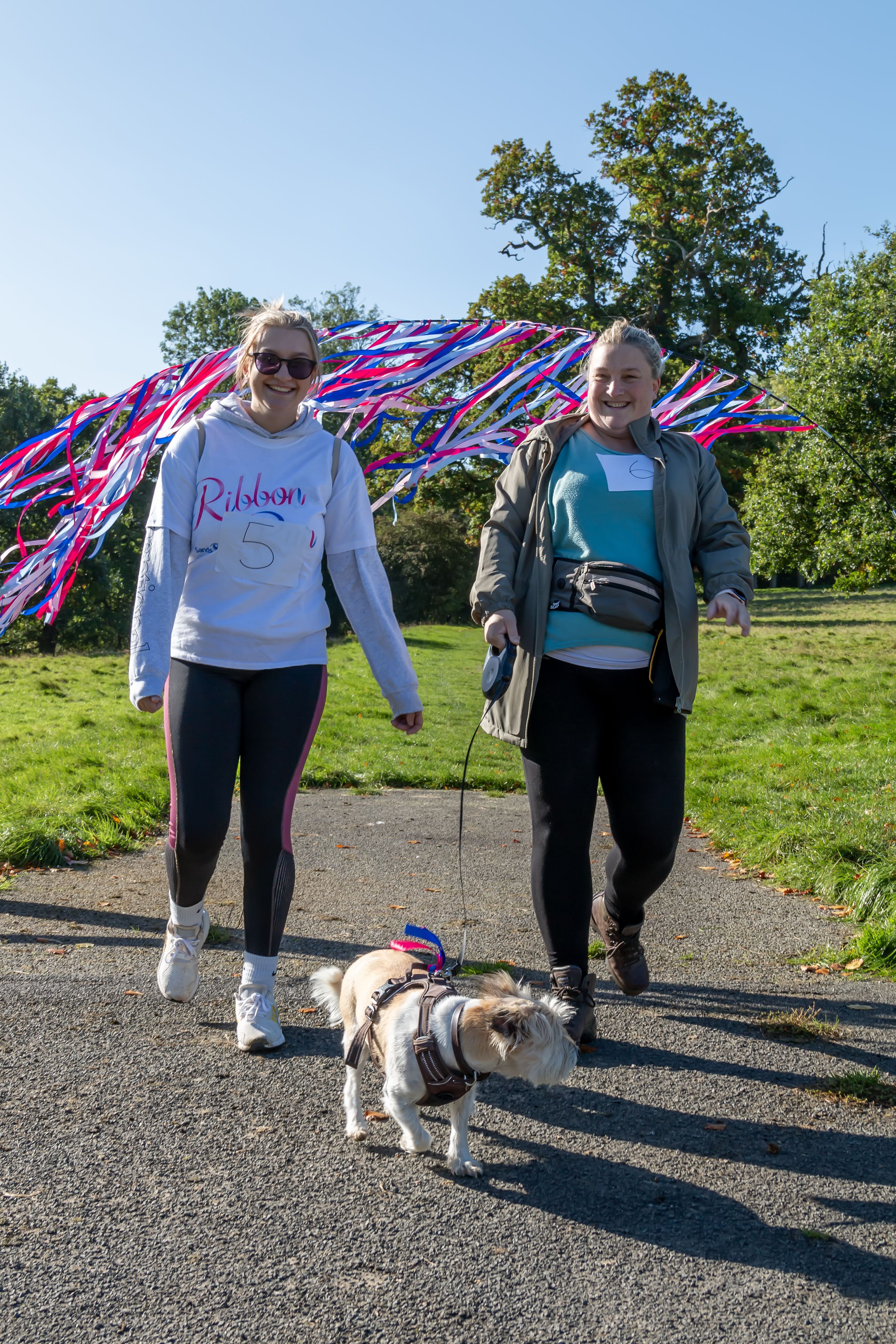 2 female Sands fundraisers taking part in Ribbon Run while walking their dog. One of the women is wearing a Ribbon Run T-Shirt.
