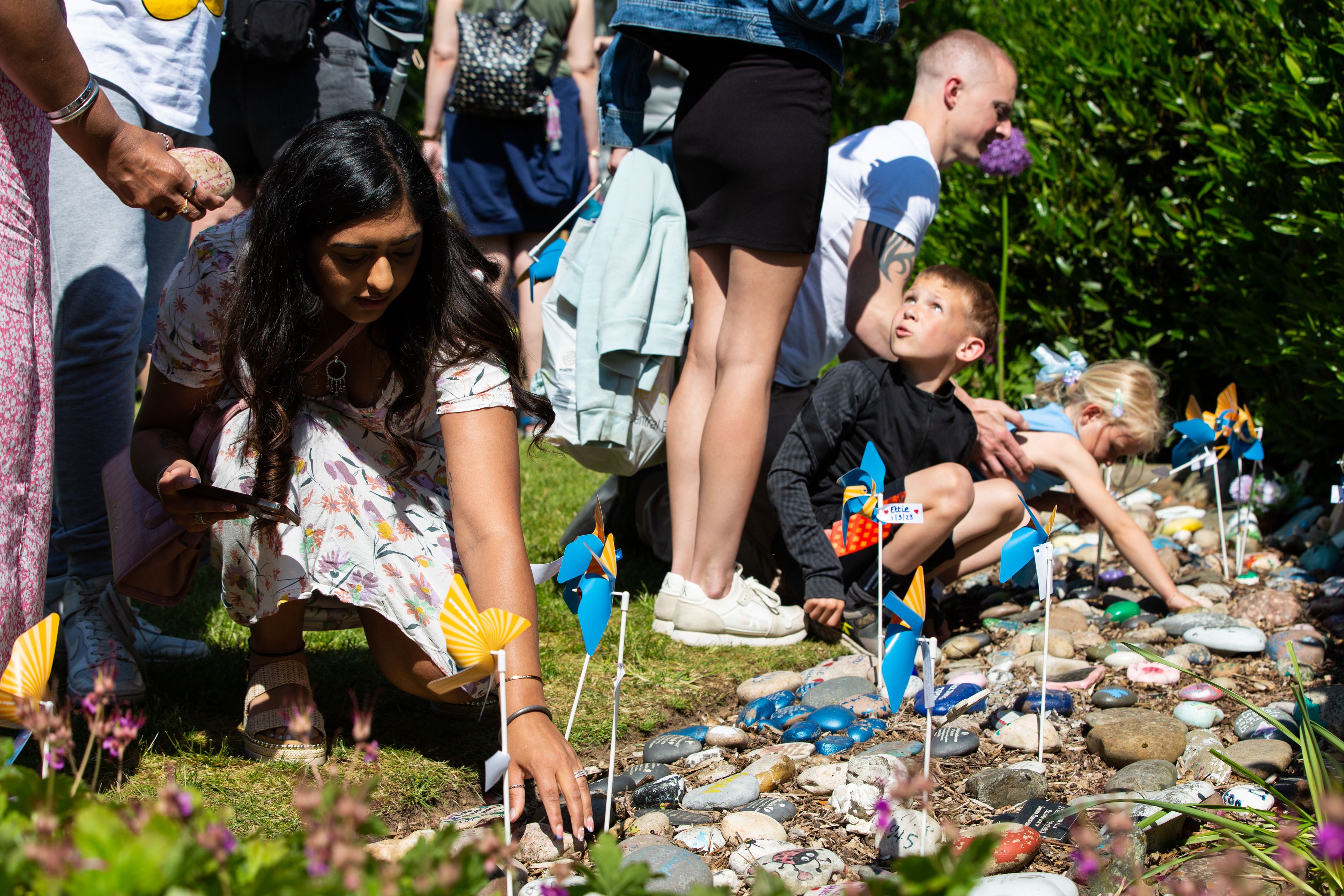 Bereaved families placing down stones and pinwheels in the Sands Garden. There is a woman on the left touching one of the stones on the ground.