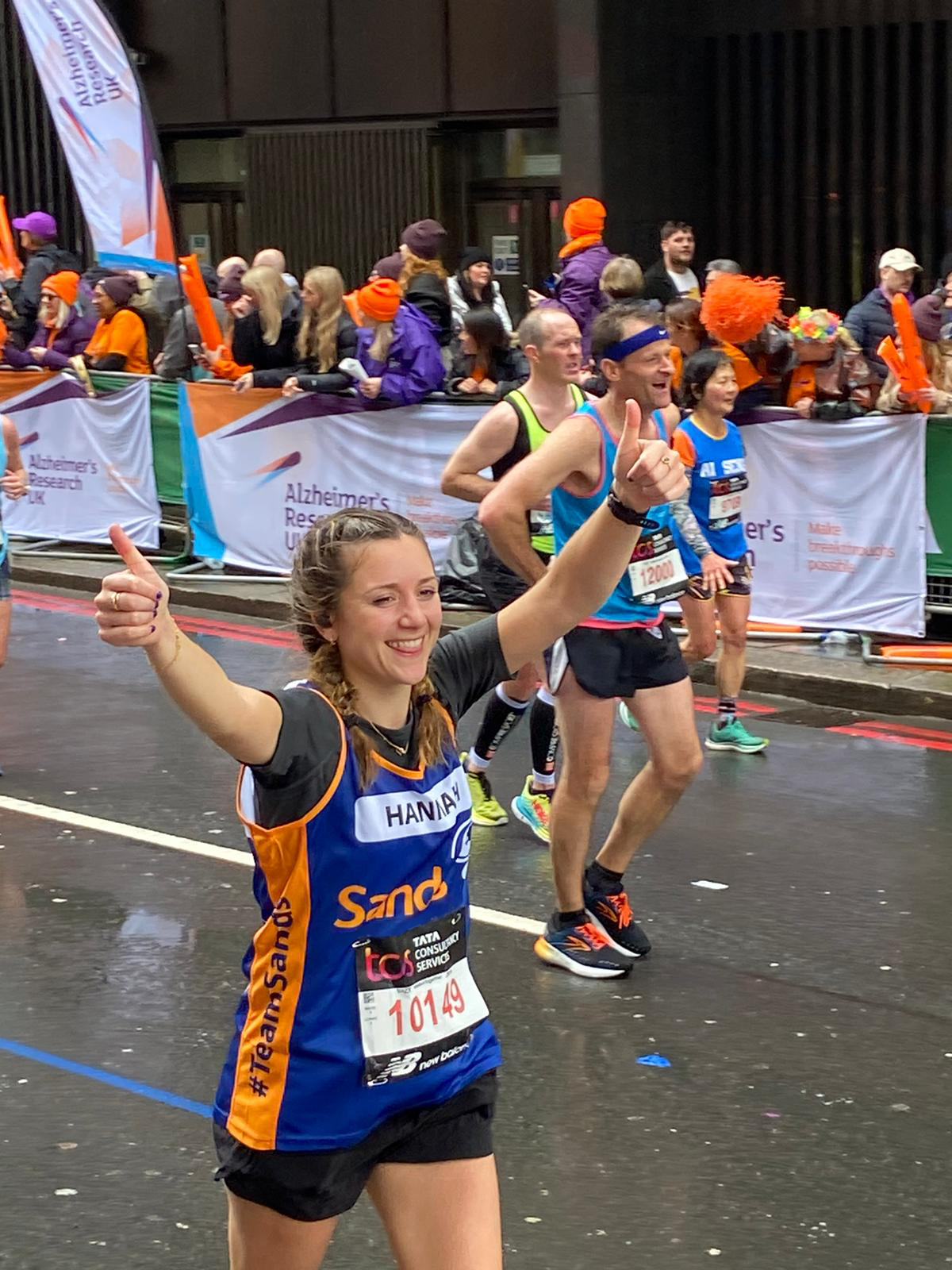 A Sands fundraiser celebrating during a marathon. She is smiling and wearing a Blue and Orange Sands Jersey.