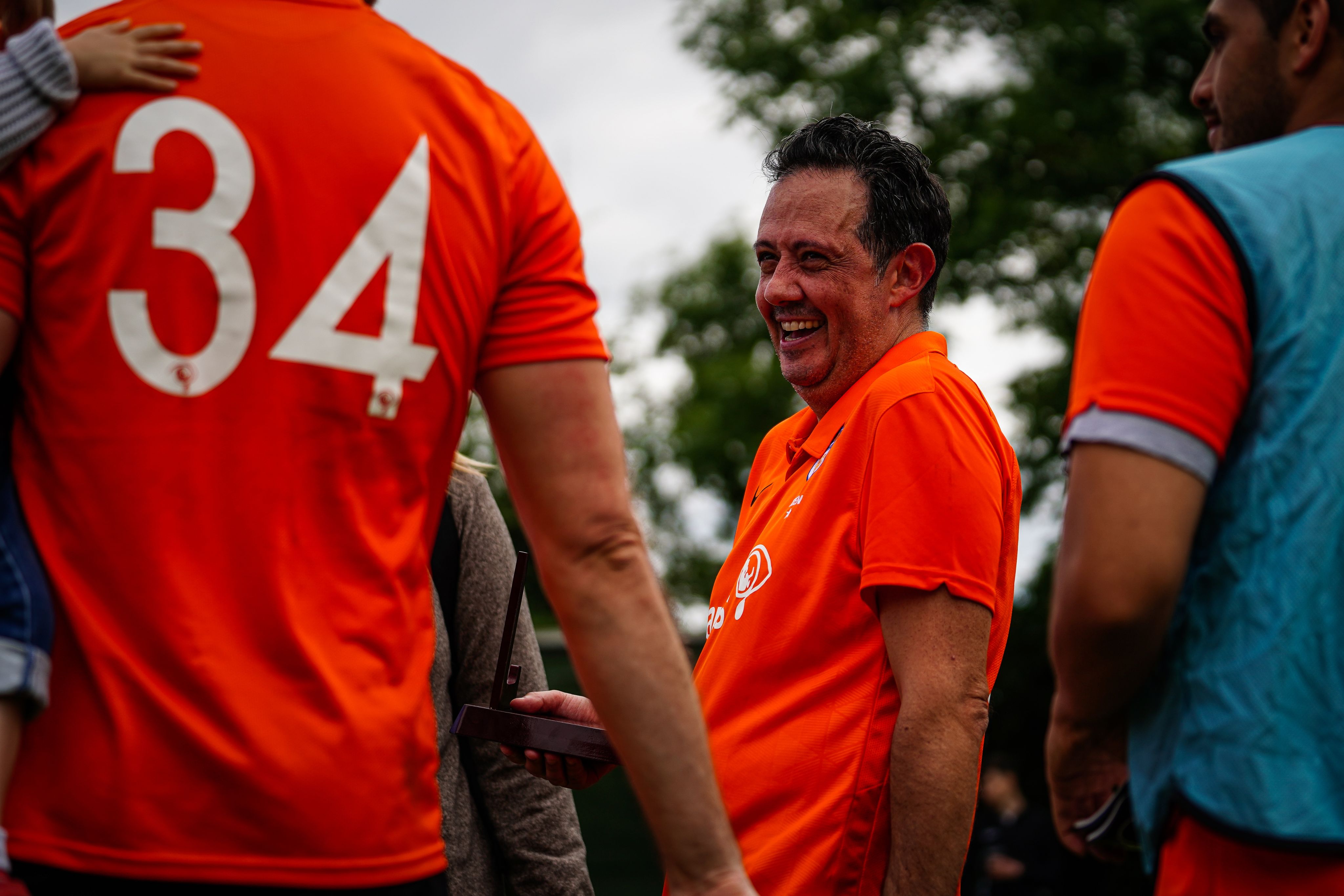 Sands United players and fathers talking and laughing. They are wearing bright orange Sands United Football Kits.