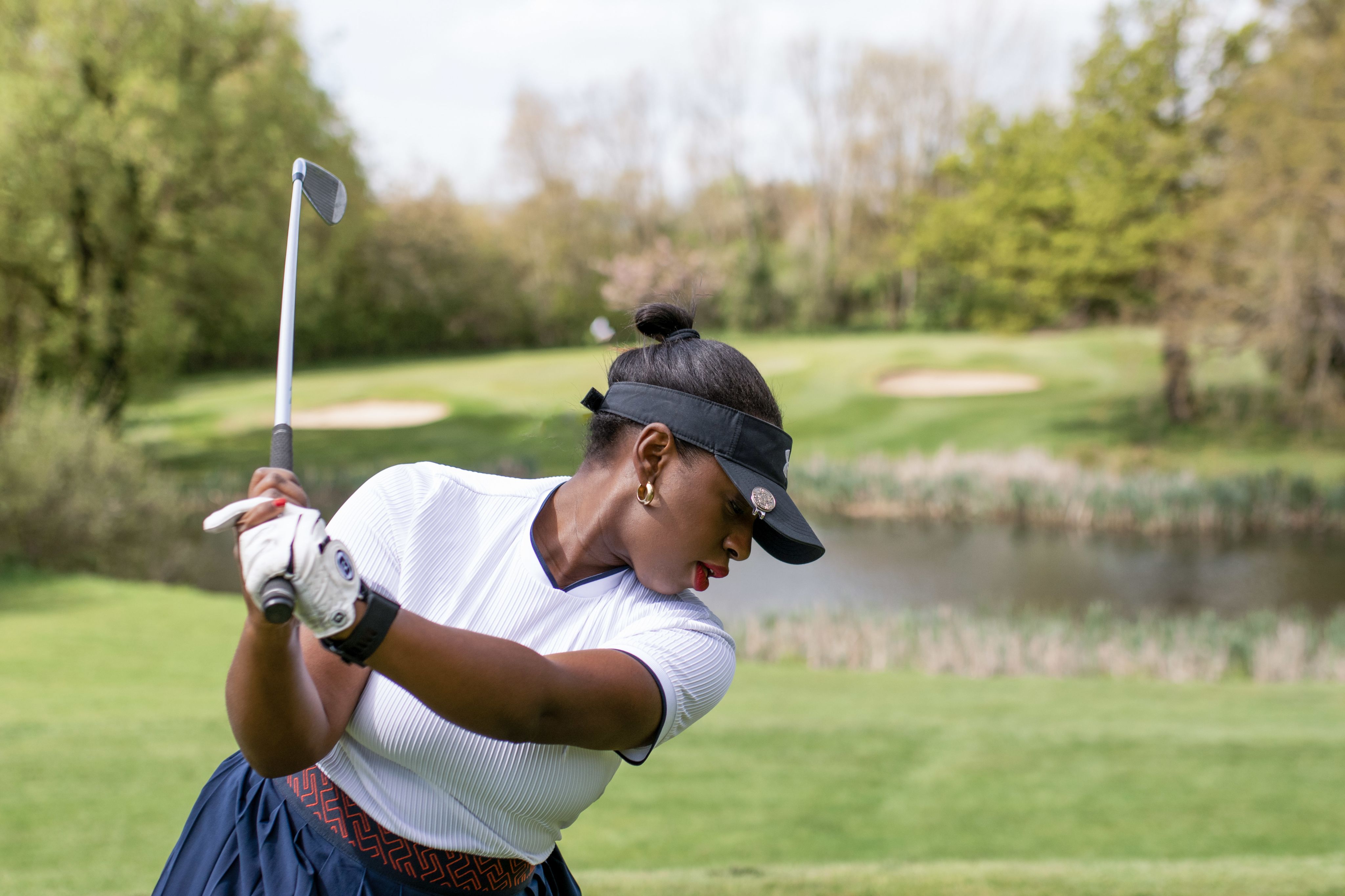Genelle playing golf in a golf course. She is mid golf swing.