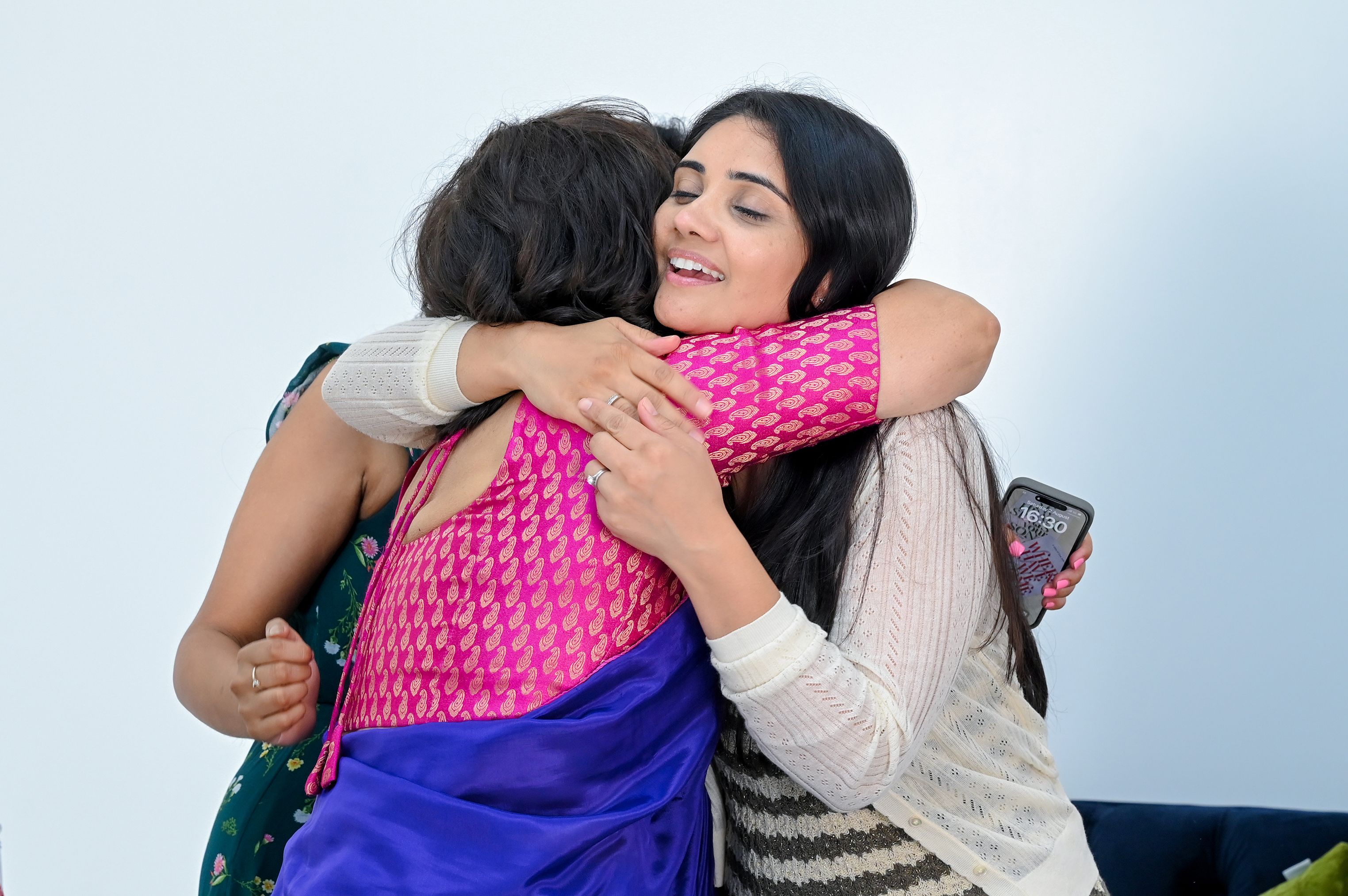 Two women embrace each other warmly in a living room filled with soft lighting. 
