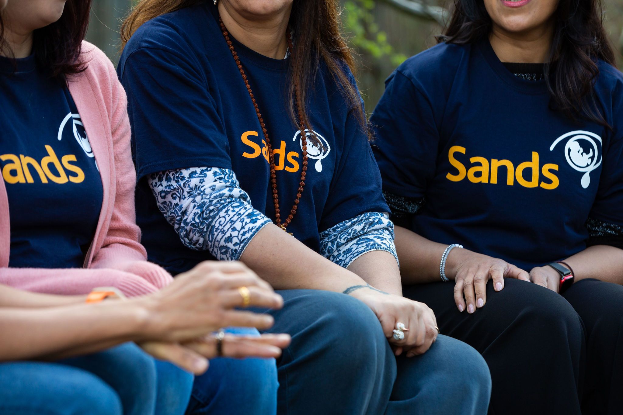4 bereaved South Asian mothers having a conversation. They are all wearing blue Sands T-shirts. 