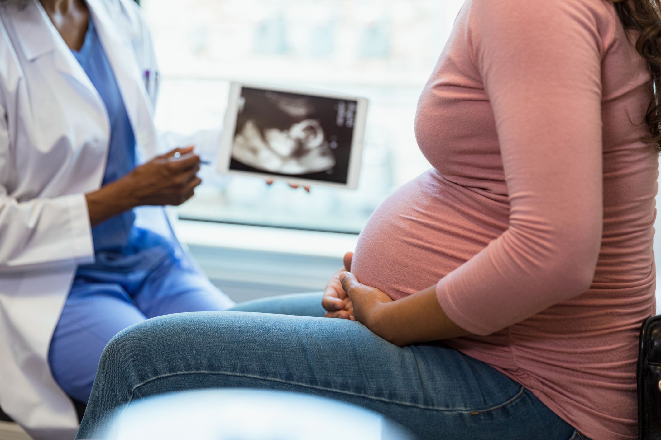 A doctor showing an ultrasound scan on a tablet to a pregnant woman.