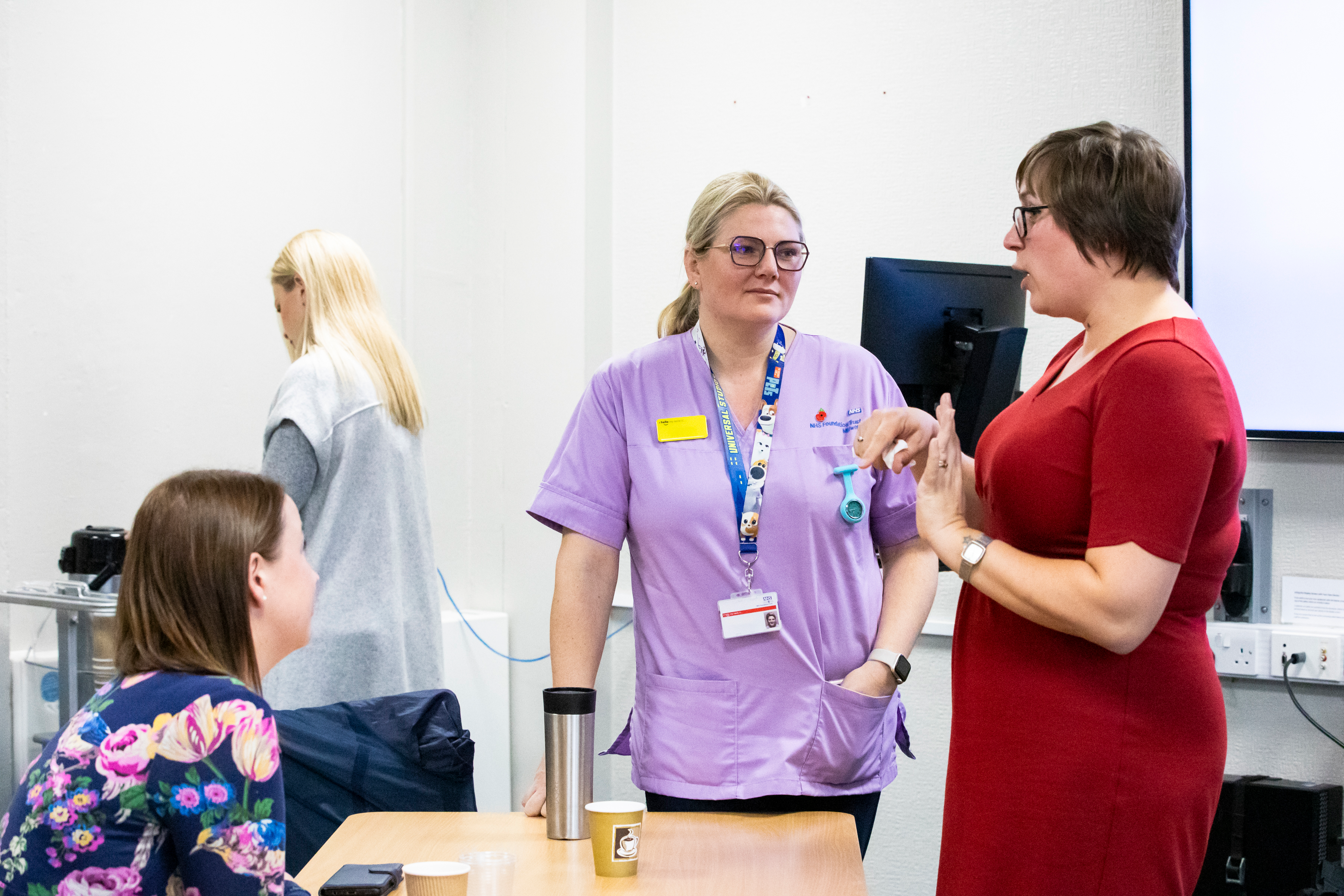 3 healthcare professionals having a conversation during a Sands Training session. The woman wearing red is speaking while the other 2 are listening.
