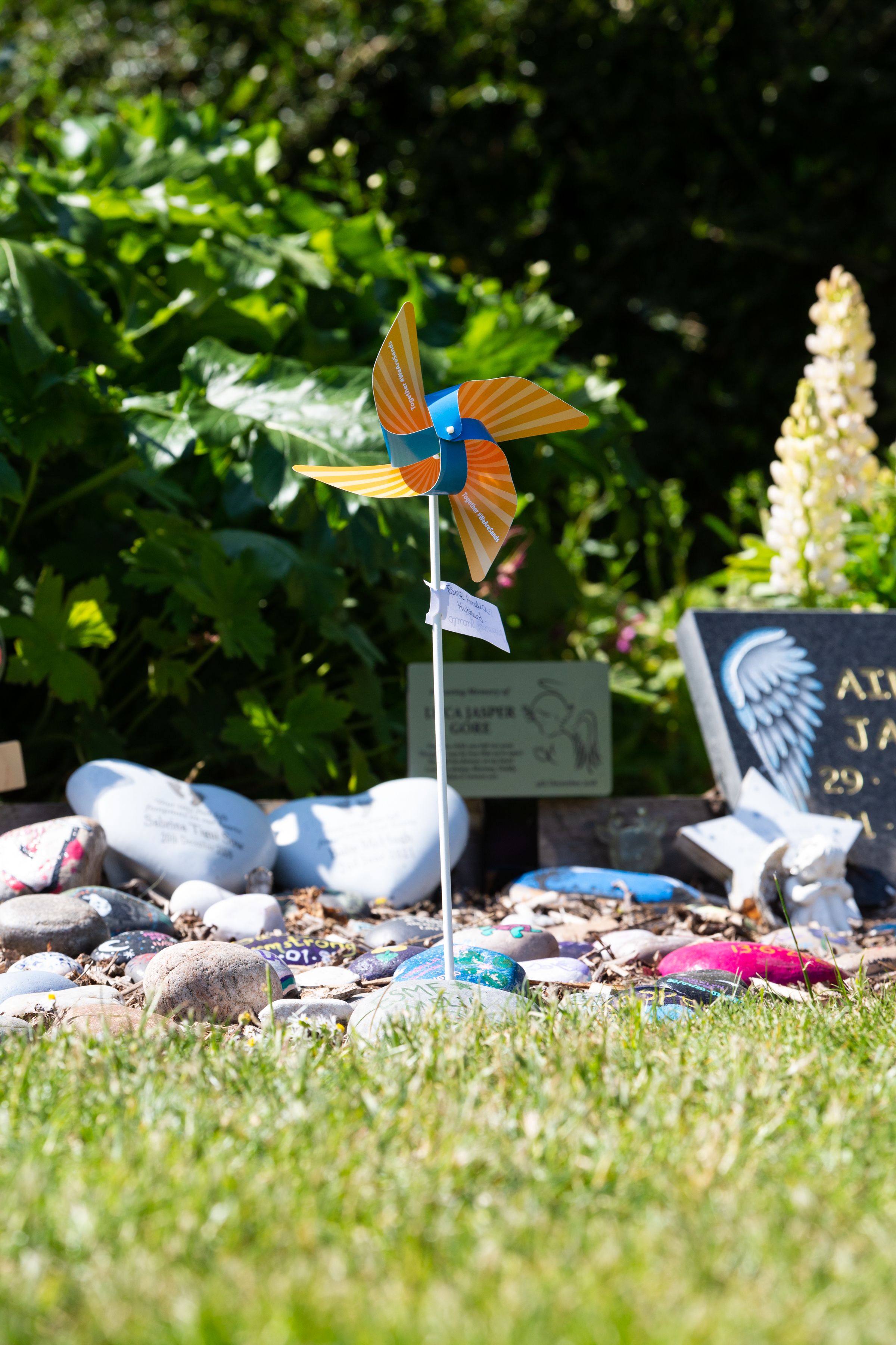 A single Sands Pinwheel standing tall in the ground in the Sands Garden surrounded by remembrance stones during Sands Garden Day 2023.