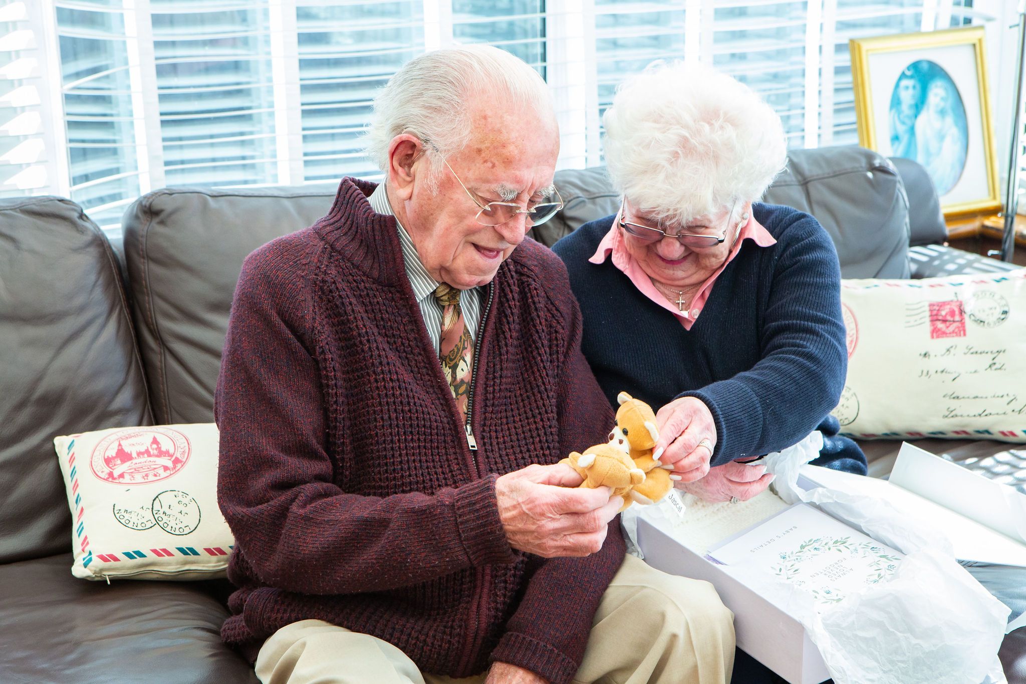 Long ago bereaved elderly couple smiling and holding teddy bears from a Sands Memory box.