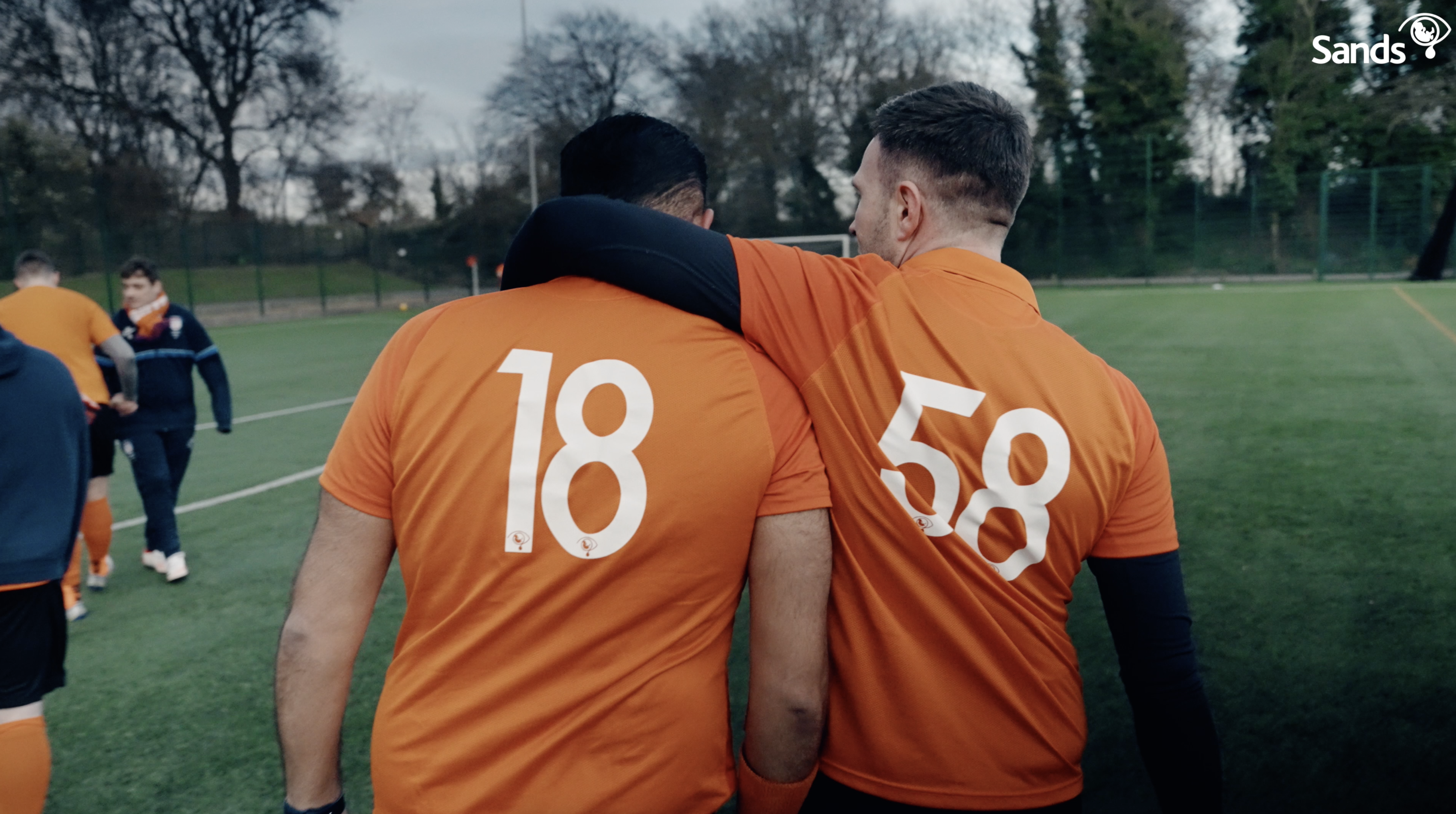Dad with his arm around the shoulder of another dad during a Sands United football game.