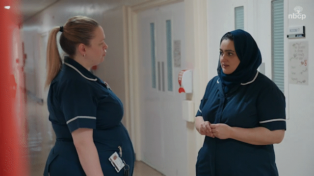 Two NHS nurses talking inside a hospital hallway.