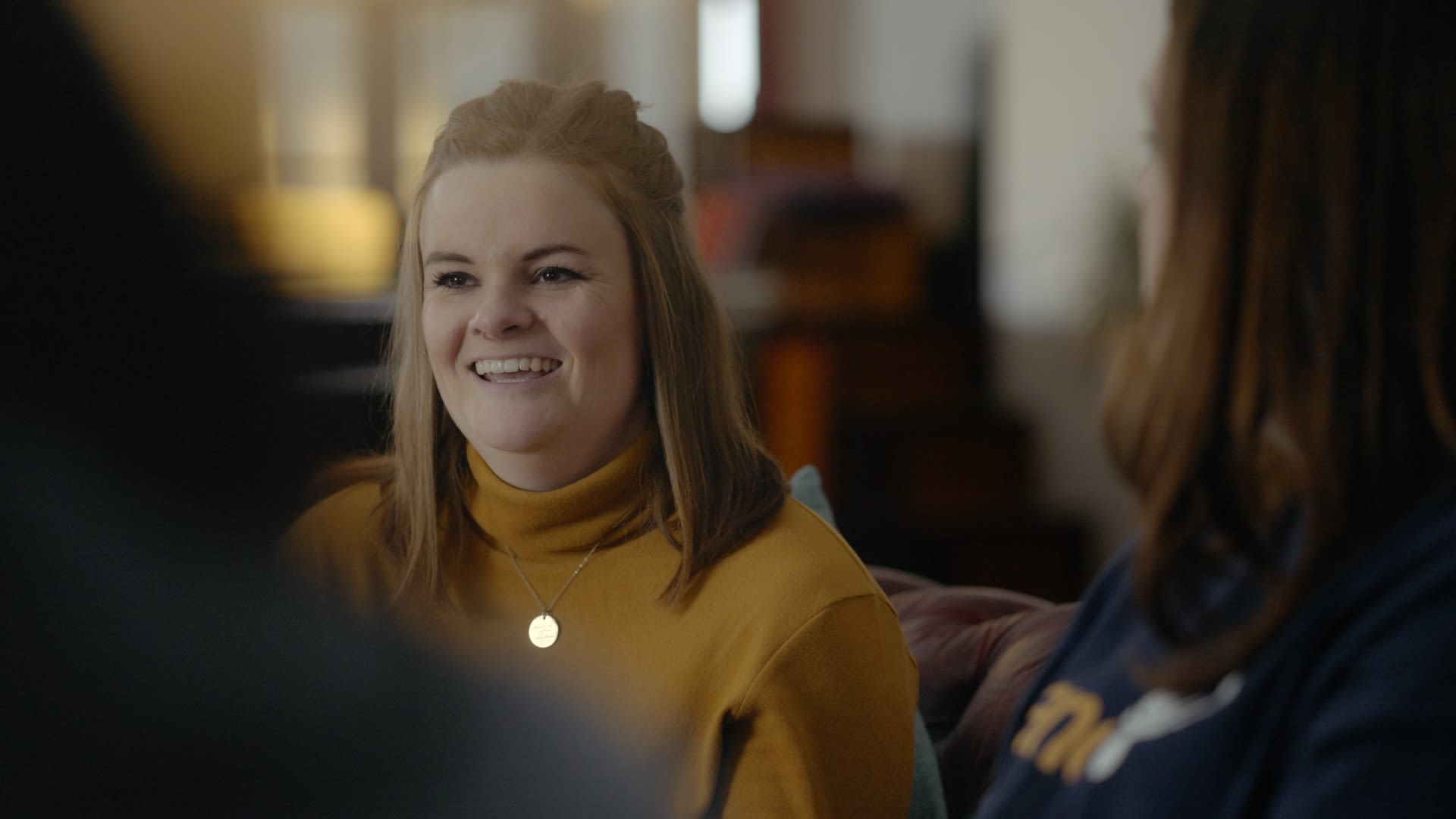 Still from the 'Become a Sands Befriender' video. Women having a conversation in a living room and smiling.