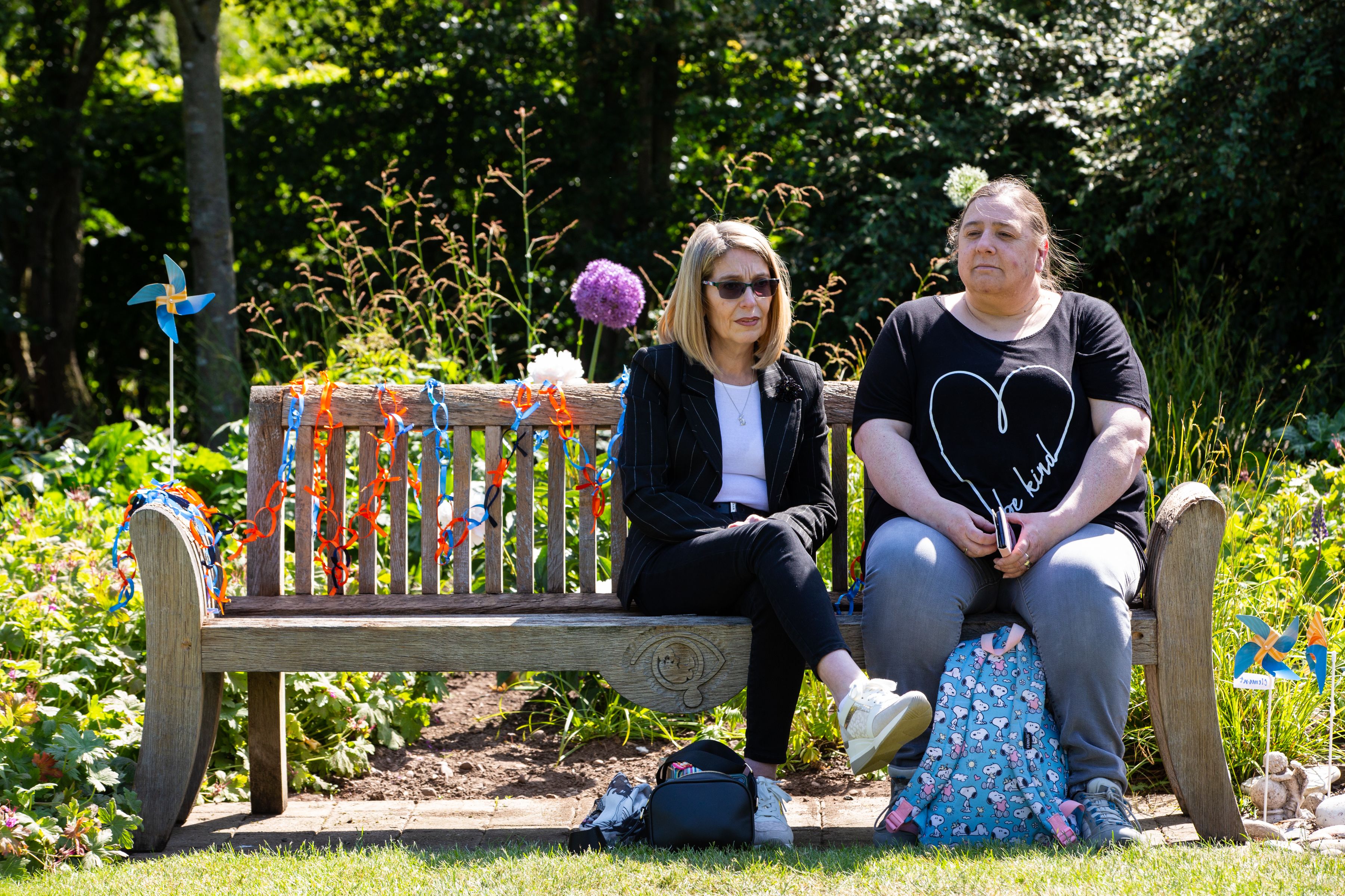2 women sitting and smiling on the Sands bench during Garden Day. Links of Orange and Blue ribbons and tied onto the bench.