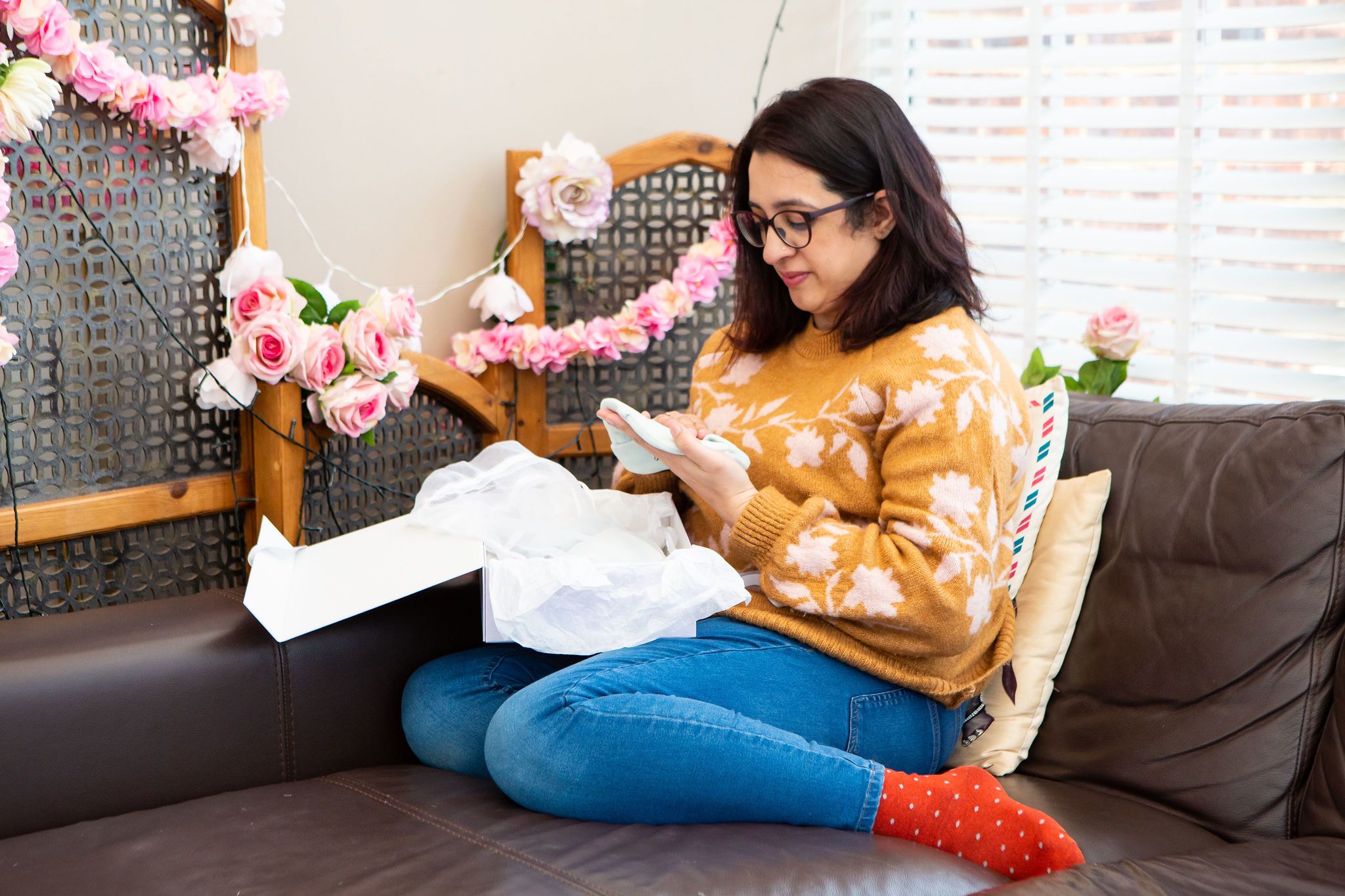 Asiya sitting on a sofa while opening a Sands Memory Box and clutching one of the items in her hands.