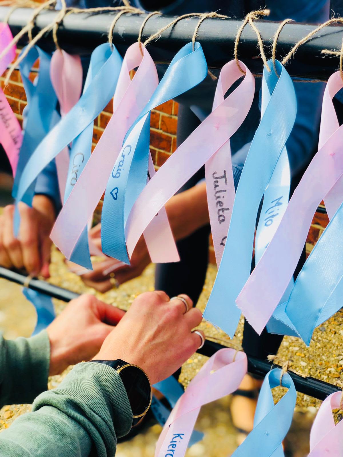 Bereaved parents tying pink and blue ribbons onto a railing. Babies names are written on the ribbons.
