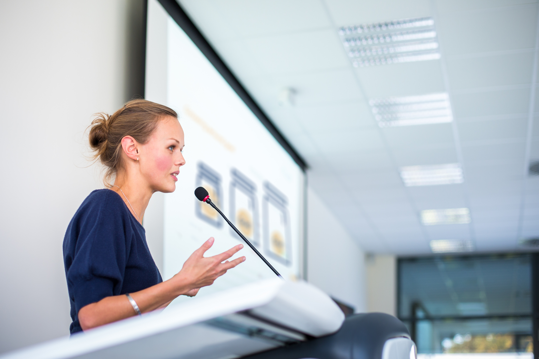 A speaker at a microphone in front of a presentation.